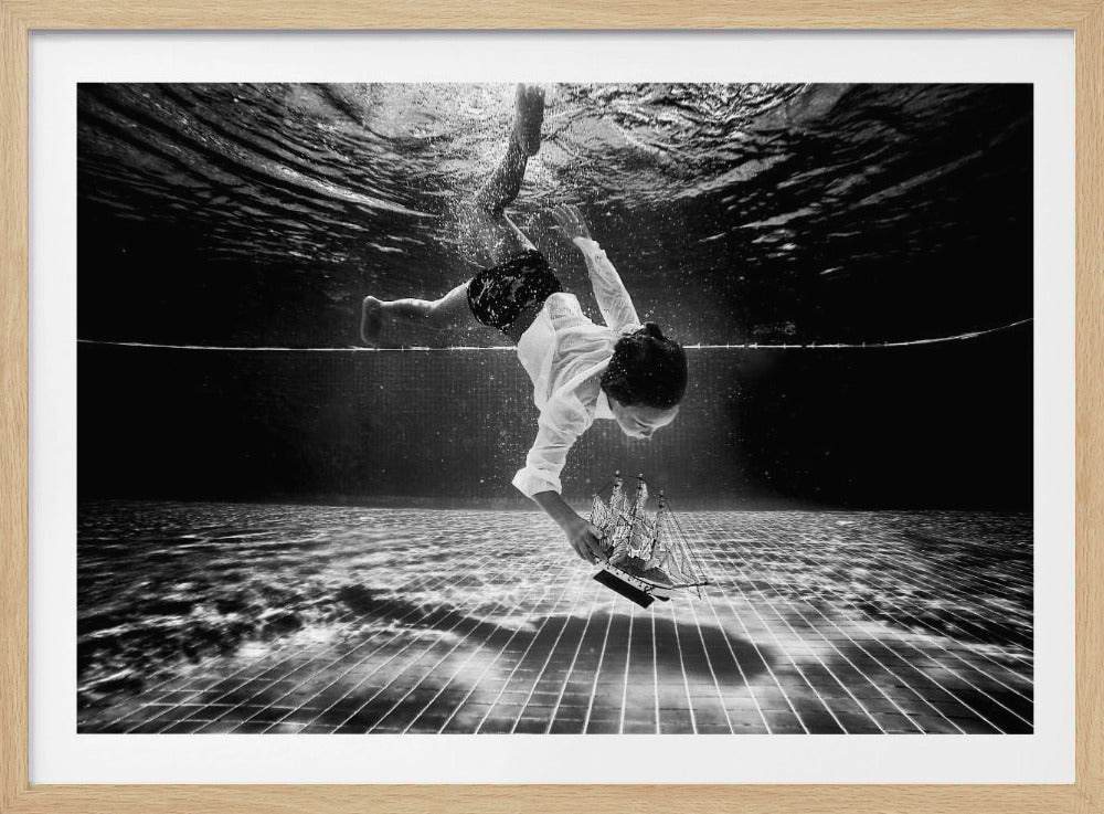 A surreal black and white underwater photograph of a child in a white shirt and shorts diving towards the bottom of a tiled pool to retrieve a miniature model of a sailing ship. Artwork