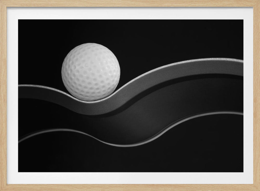 A framed, minimalist black and white photograph of a golf ball resting on a gracefully curving gray surface against a solid black background. Wall Art