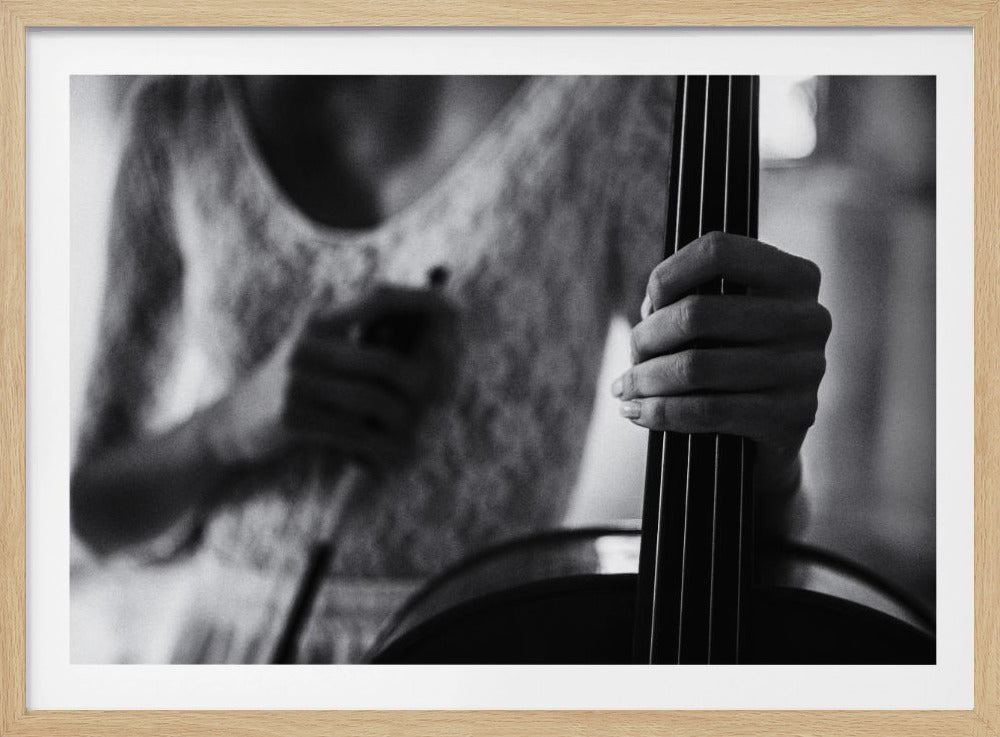 A grainy, black and white close-up photo focusing on a musician's hand firmly gripping the neck and strings of a cello. The player's body is out of focus in the background, creating a shallow depth of field. The entire image is enclosed in a brushed silver frame. Wall Art