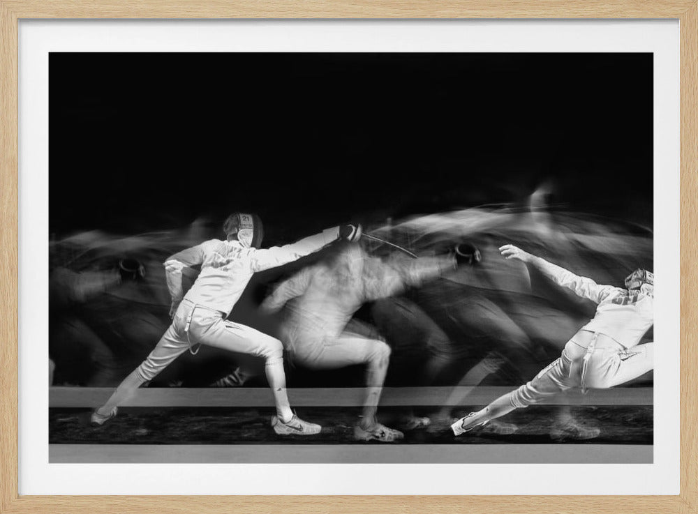 A framed, dramatic black and white photograph using long exposure to capture a fencer in motion. The fencer, in full white gear, lunges forward, their form crisp at the end of the movement while a ghostly blur trails behind, illustrating their rapid advance against a black background. Decor