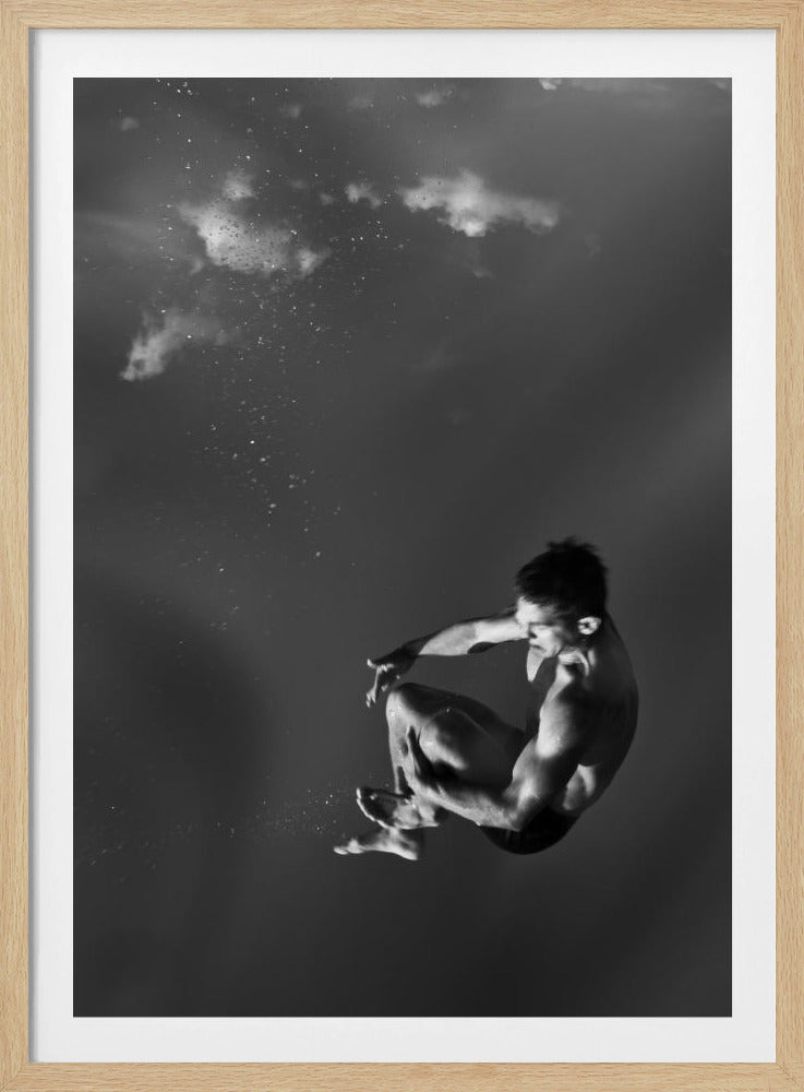 A dramatic black and white photograph of a male diver suspended mid-air in a tuck position. The background is a dark, atmospheric gray, with what appears to be clouds and bubbles, giving the impression of being underwater or in a vast, empty space. The lighting highlights the athlete's muscular physique. Artwork