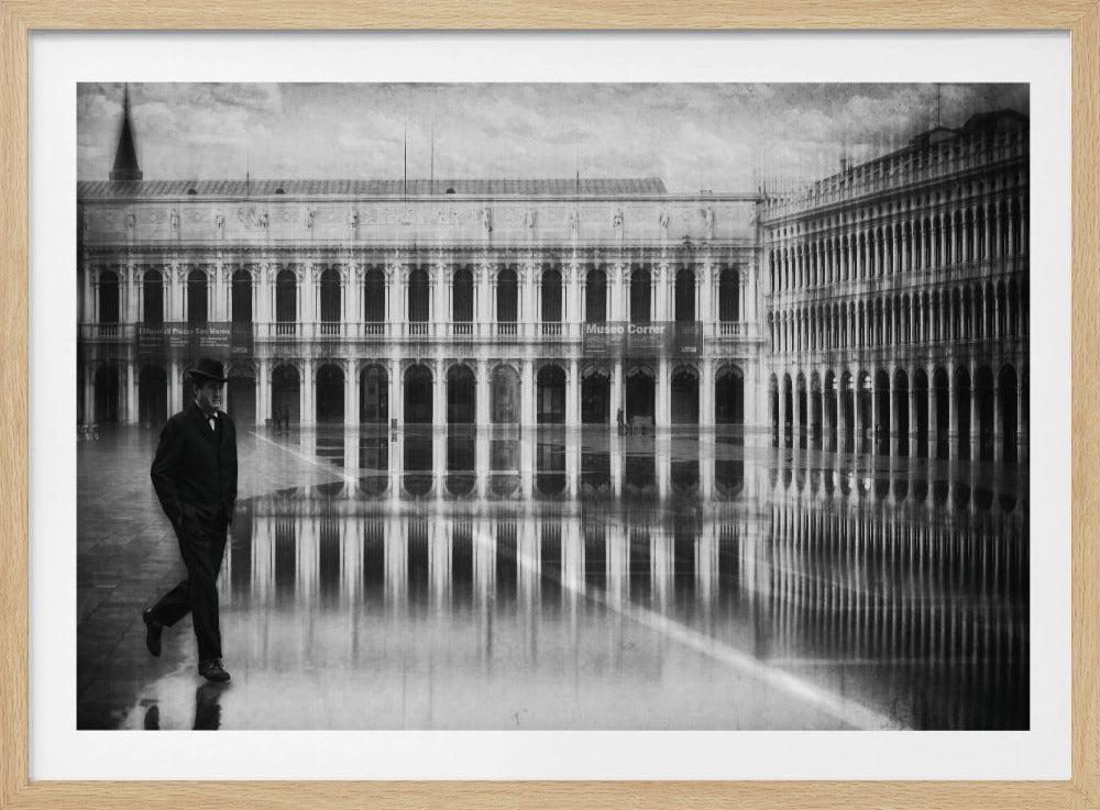 A vintage-style, black and white photograph of a man in a dark suit and hat walking through a flooded St. Mark's Square in Venice, with the grand arched buildings reflected in the water-covered ground. The image has a textured, aged look and is displayed in a silver frame. Artwork