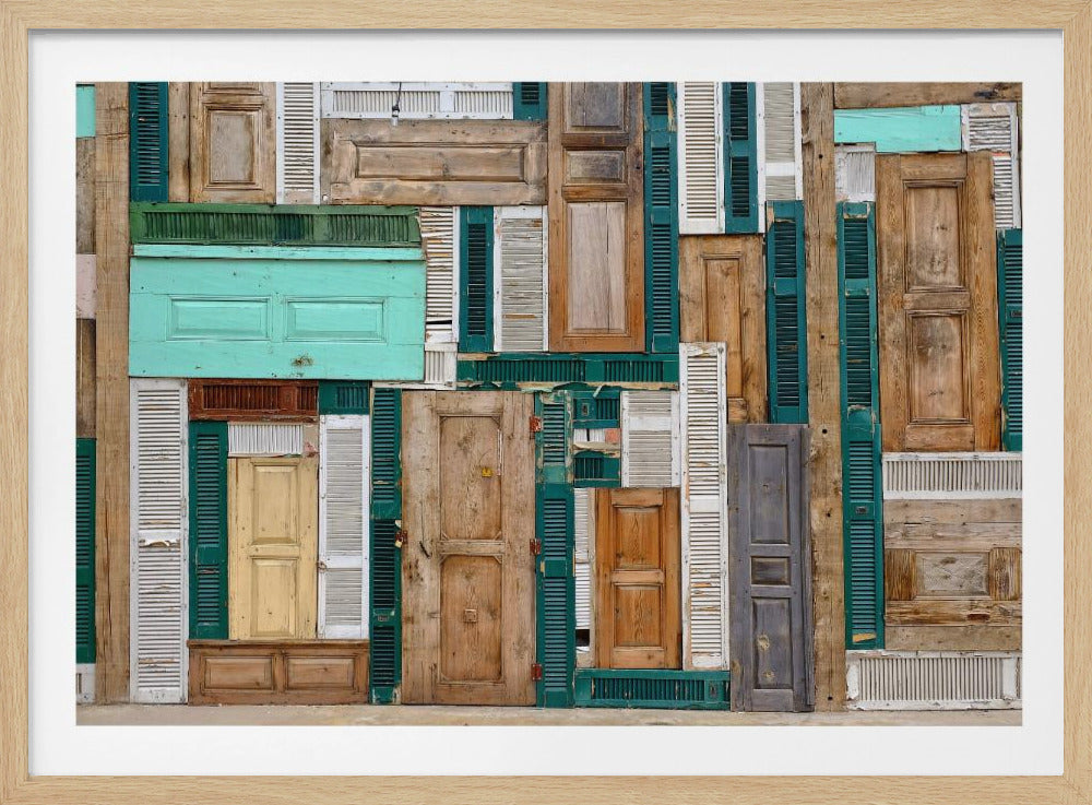 A framed art piece featuring a chaotic collage of various old, weathered wooden doors and window shutters arranged in a dense patchwork, showcasing a rustic texture and colors like natural wood, teal, green, and distressed white. Wall Art