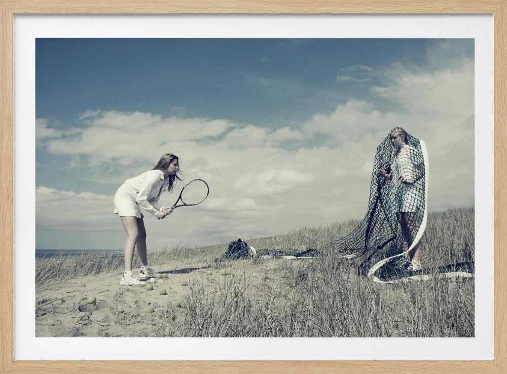A surreal photograph of two women on a grassy sand dune. One woman is dressed in white tennis attire, bent over and ready to hit a ball with her racket. The other woman stands opposite her, entangled and draped in a large tennis net. The scene is under a cloudy blue sky and has a desaturated, cool-toned color palette, framed in silver. Decor