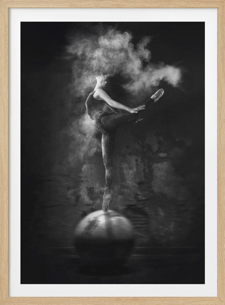 A dramatic black and white photograph of a ballerina balancing en pointe on a large sphere. Her body is arched back in an elegant pose as a cloud of white powder explodes around her, her long hair flying through the air. Wall Art