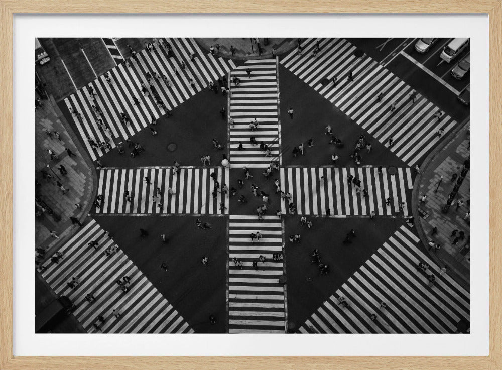 A framed, high-angle, black and white photograph capturing the iconic Shibuya Crossing in Tokyo. The symmetrical composition highlights the geometric pattern of the multiple wide crosswalks, with numerous pedestrians scattered across them, creating a sense of organized chaos. Artwork