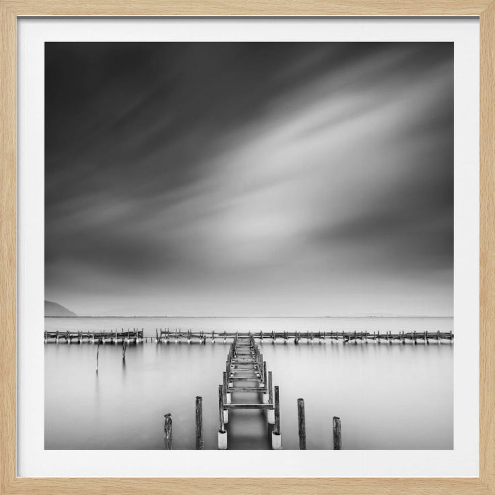 A framed, square black and white long-exposure photograph of a dilapidated wooden pier extending into calm, misty water. The sky is filled with soft, streaked clouds, creating a serene and melancholic mood. Wall Art