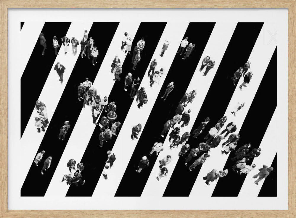 A striking black and white aerial photograph of dozens of people walking across a large, diagonally striped crosswalk. The high-contrast, graphic pattern of black and white stripes dominates the scene, with the small figures of pedestrians scattered across it, creating a sense of movement and urban anonymity. The image is presented within a simple silver frame. Print