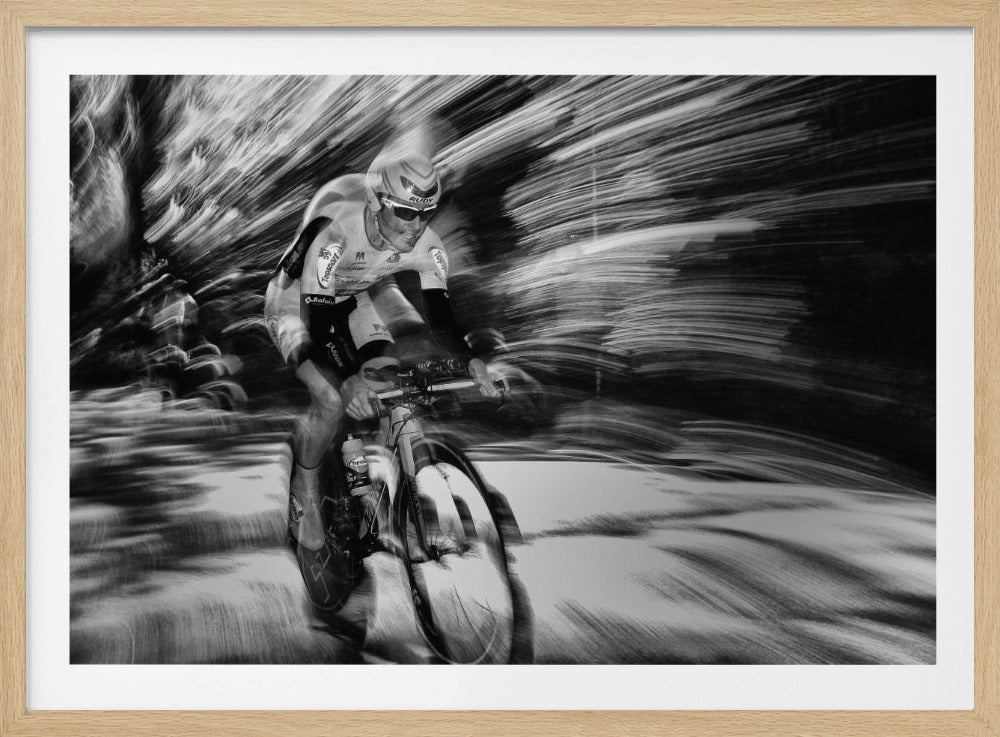 A dramatic black and white action shot of a professional cyclist racing. The cyclist is in focus, wearing a helmet and sunglasses, while the background is a streaky motion blur, creating a powerful sense of speed and movement. The image is enclosed in a silver frame. Wall Art