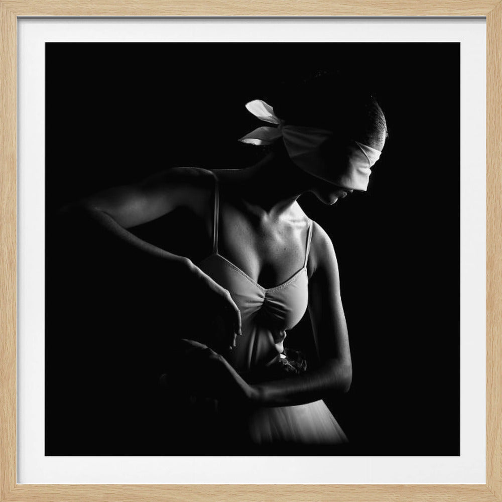 A dramatic black and white photograph of a ballerina wearing a blindfold, posing gracefully. The lighting creates a strong contrast with deep shadows, highlighting her form against a black background. The image is presented within a light-colored wooden frame. Poster