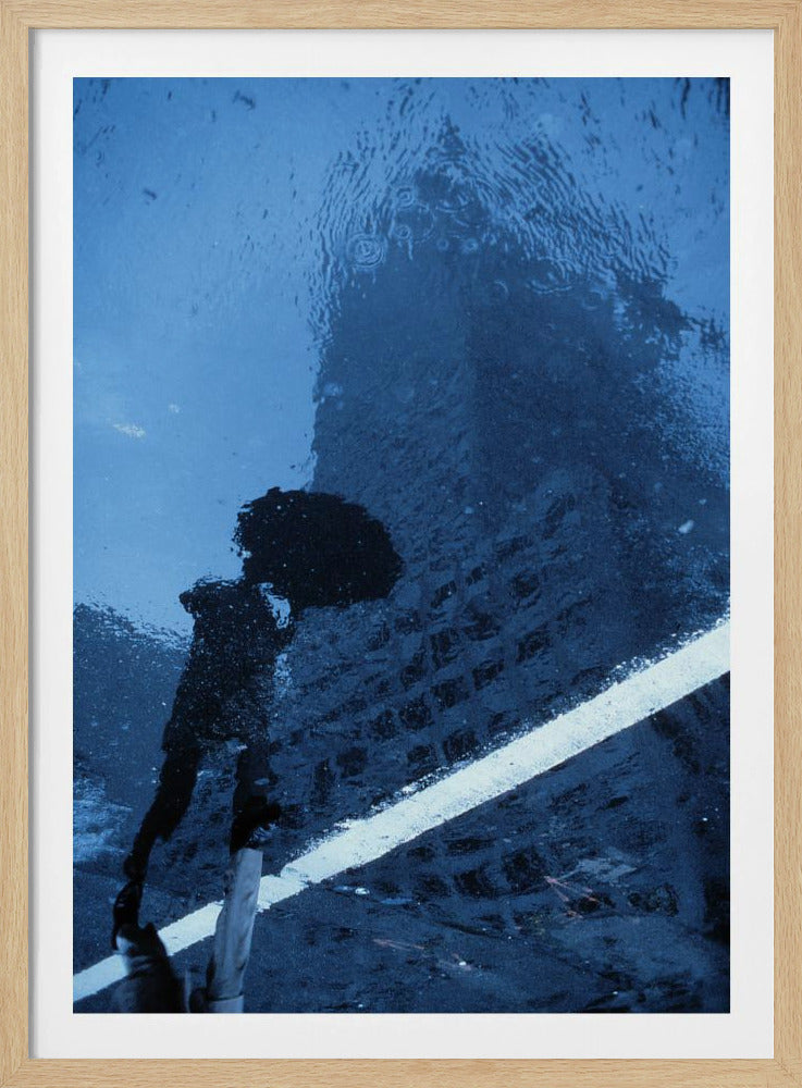 A moody, blue-toned photograph of a reflection in a rainy puddle. A black silhouette of a person holding an umbrella and a distorted brick building are visible, with a single white line crossing the wet street. Poster
