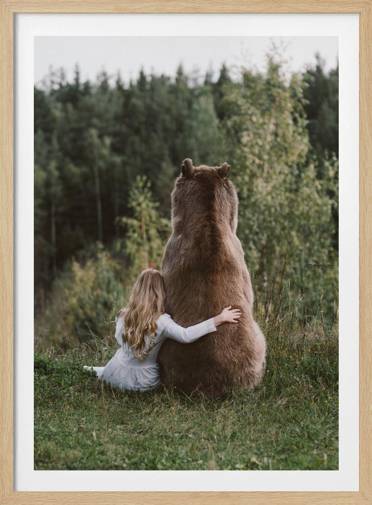 A gentle photograph from behind of a young girl with long blonde hair hugging a large brown bear. They are both sitting in a grassy field, facing a dense green forest in the background. Artwork
