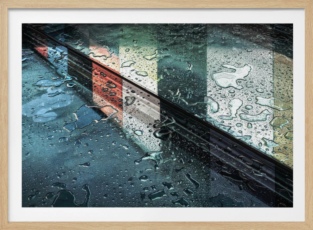 An abstract close-up photograph of a wet, dark surface, possibly a car, covered in raindrops, with a prominent black diagonal line. Colorful vertical stripes of red, cream, and green are reflected on the glossy, wet surface. The artwork is presented in a silver frame. Decor