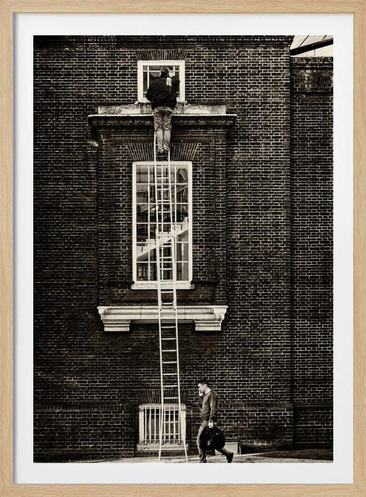 A striking black and white photograph of a man cleaning a small window high up on a brick building, standing precariously at the top of a very long ladder. Below, another man walks past on the street, seemingly unaware of the scene above. Artwork
