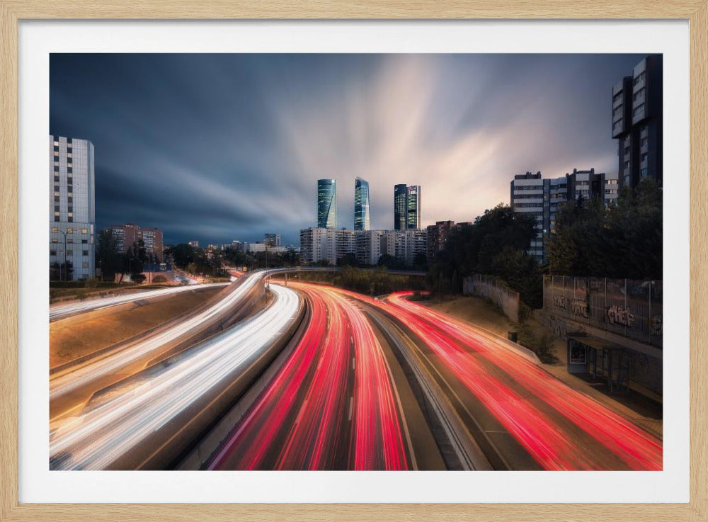 A long-exposure photo of a curving city highway at dusk, where car lights create vibrant red and white streaks leading towards a modern skyline with towering skyscrapers under a dramatic sky. Poster