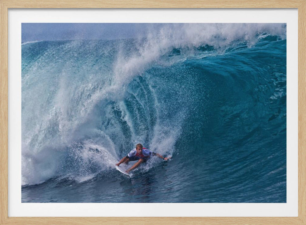 A dramatic action shot of a professional surfer skillfully navigating the inside of a massive, curling blue ocean wave, surrounded by white sea spray, all enclosed in a silver frame. Artwork