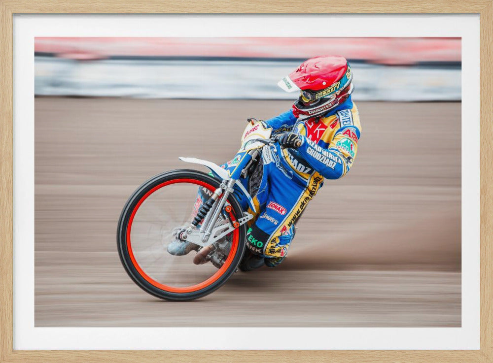 A speedway motorcycle racer in a blue and yellow suit with a red helmet leans sharply into a turn on a dirt track, with motion blur in the background conveying a sense of high speed. Print