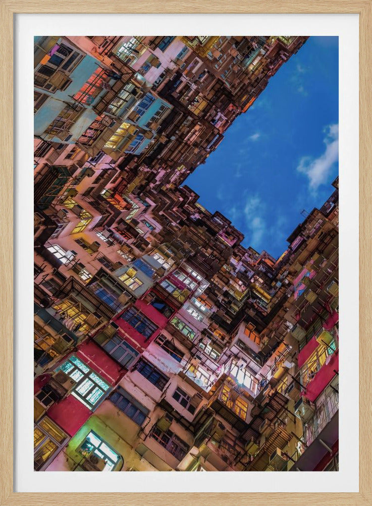 A dramatic worm's-eye view looking up at colorful, densely packed high-rise apartment buildings that create a geometric frame around a patch of deep blue sky. Wall Art