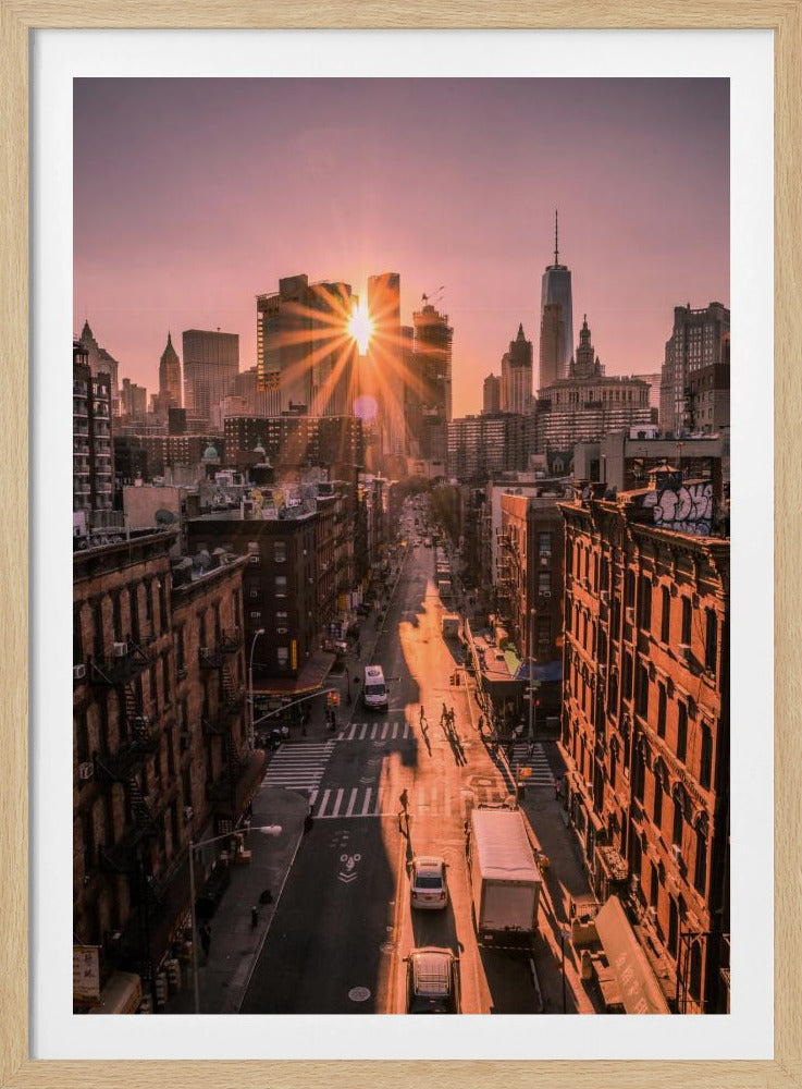A high-angle view of a New York City street at sunset, with the sun bursting between skyscrapers and casting long golden shadows over the buildings and traffic below. Decor