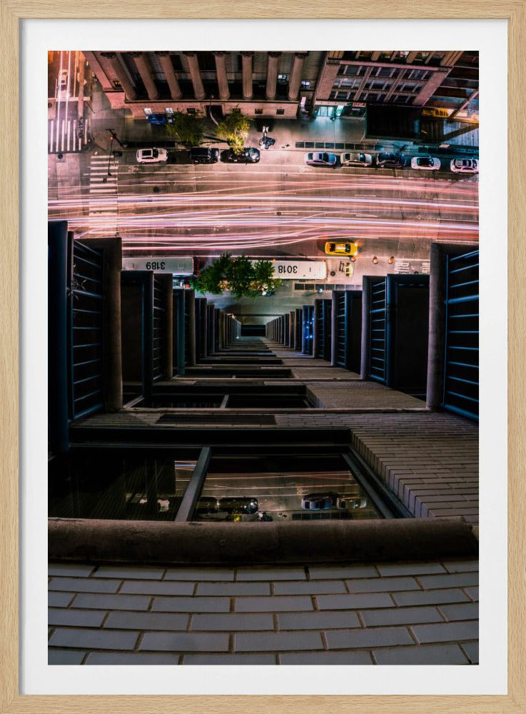 A dizzying bird's-eye view looking straight down the side of a skyscraper into a busy city street at night, with long exposure light trails from traffic creating streaks of red and white below. Wall Art
