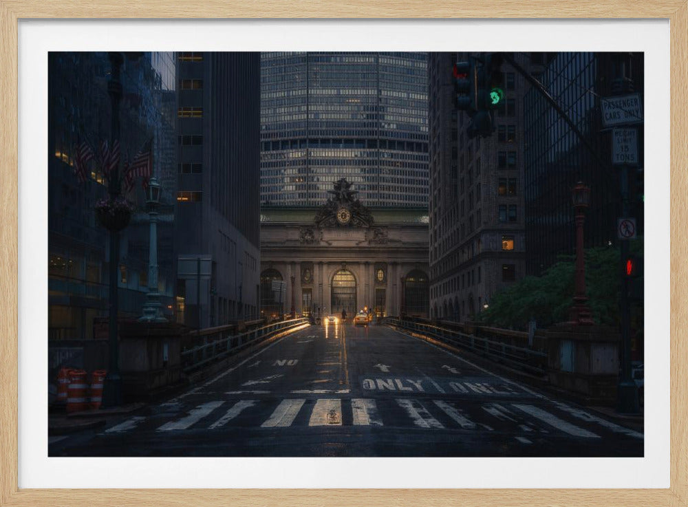 A moody photograph of a wet city street at dusk, leading towards the illuminated facade of Grand Central Terminal in New York City, which is framed by tall, modern skyscrapers. Decor
