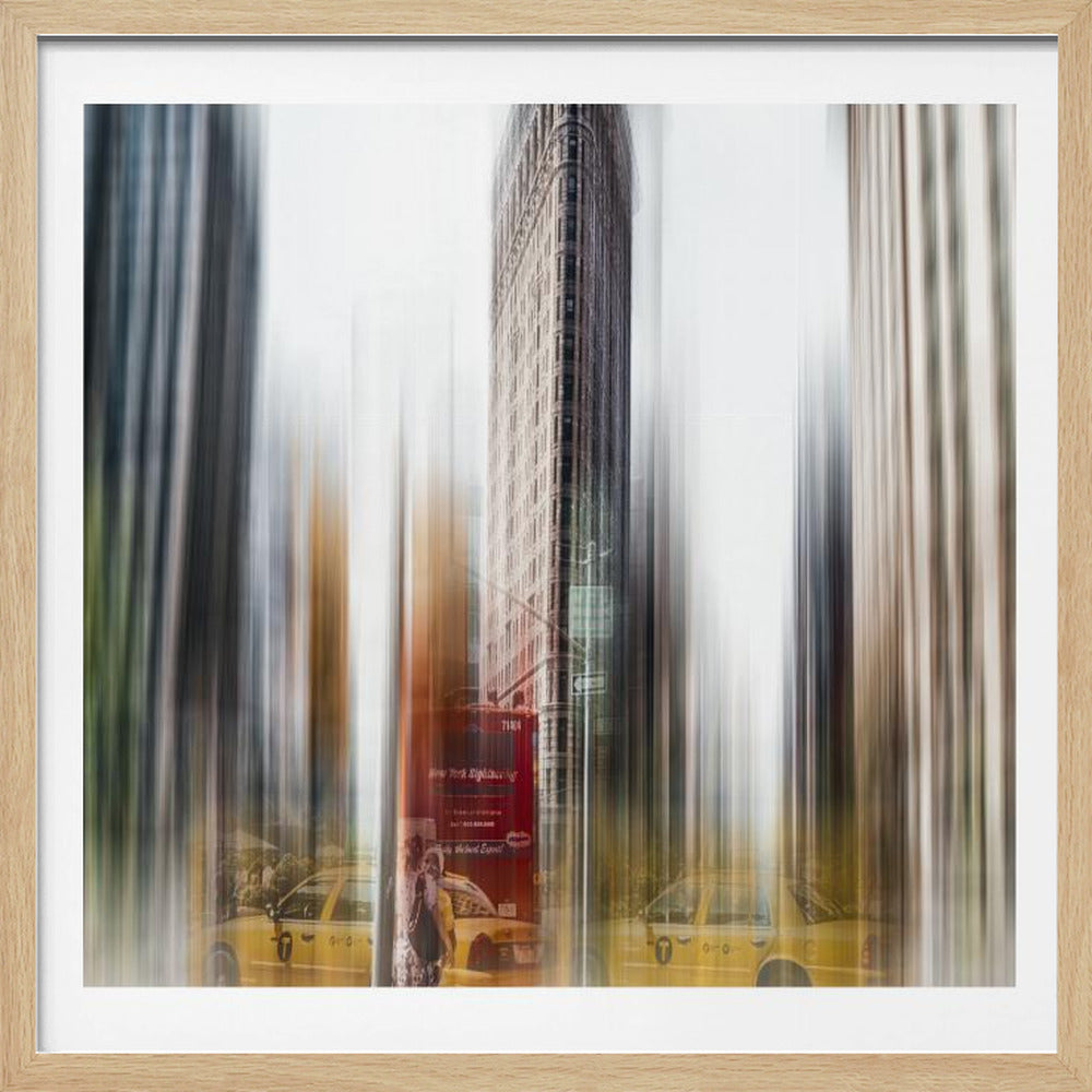An artistic photograph of New York City's Flatiron Building in a light wood frame. The image has a strong vertical motion blur effect, creating streaks of yellow from taxi cabs and gray from the surrounding architecture, capturing the bustling energy of the city. Poster