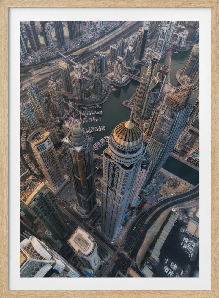 An aerial, bird's-eye view of the dense Dubai Marina, with towering skyscrapers casting long shadows. A waterway snakes through the urban canyon, with numerous yachts docked in the marina. A prominent skyscraper with a distinctive golden dome stands in the foreground. Artwork