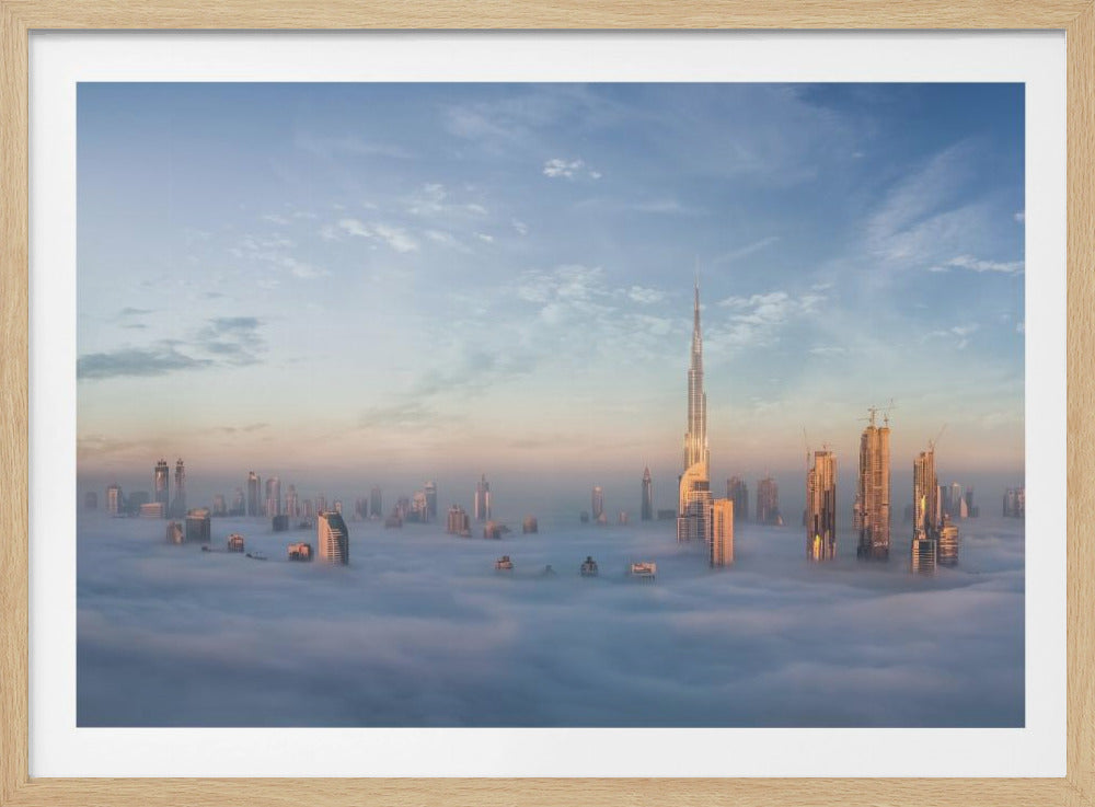 A framed photograph of the Dubai skyline, with the Burj Khalifa and other skyscrapers piercing through a thick blanket of low-lying clouds or fog. The scene is bathed in the warm, golden light of sunrise or sunset against a pale blue sky. Poster