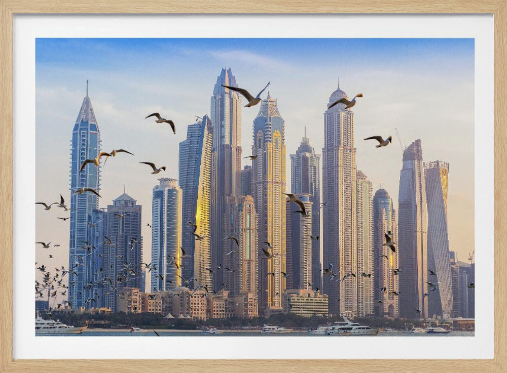 A framed artwork of the Dubai city skyline, featuring modern skyscrapers bathed in the golden light of sunset. A flock of seagulls flies in the foreground above the water, where several yachts are docked. Artwork
