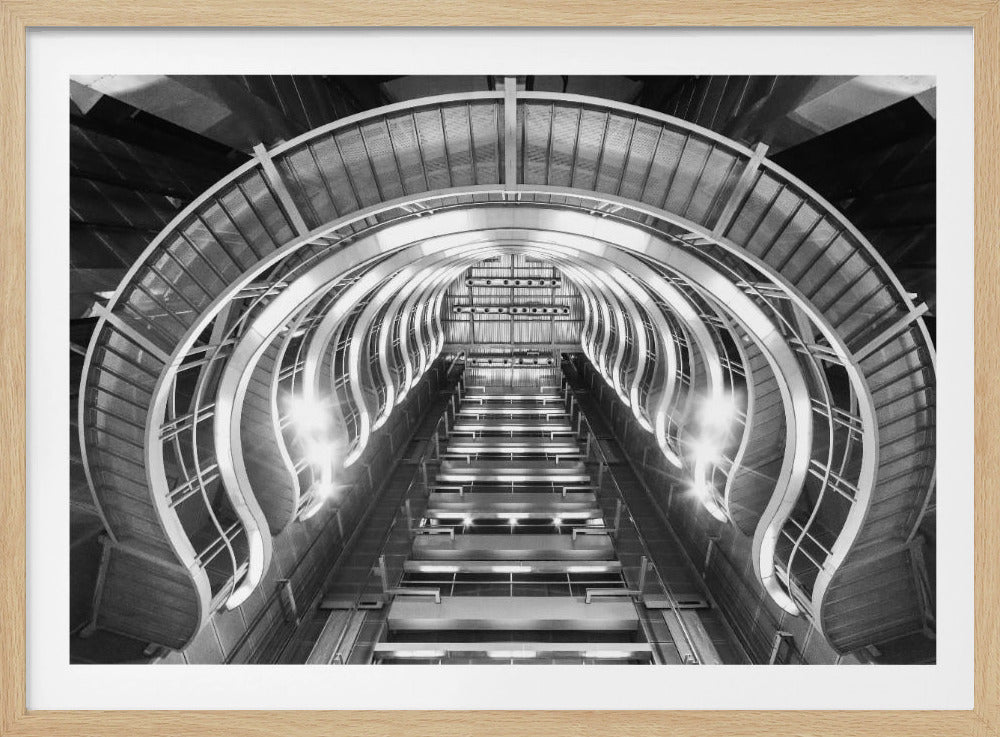 A symmetrical, low-angle black and white photograph of a futuristic escalator or grand staircase. The structure features illuminated, repeating curved arches on both sides, creating a tunnel-like perspective leading upwards. The image is presented within a silver-colored frame. Artwork