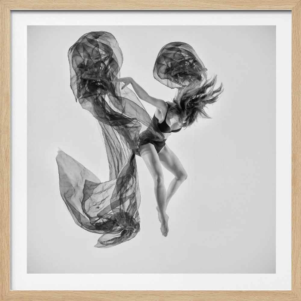 A framed black and white photograph of a female dancer in a dynamic mid-air pose. She is dressed in dark lingerie and is surrounded by a large, swirling piece of sheer black fabric that billows around her against a plain white background. Wall Art