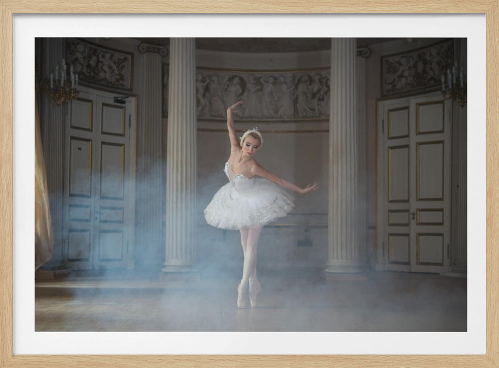 A framed photograph of a graceful ballerina in a white tutu and tiara dancing on pointe in a grand, classical hall. The room is filled with soft, white smoke and features large columns, ornate doors, and decorative wall friezes. The entire scene is captured within a silver-colored frame. Print