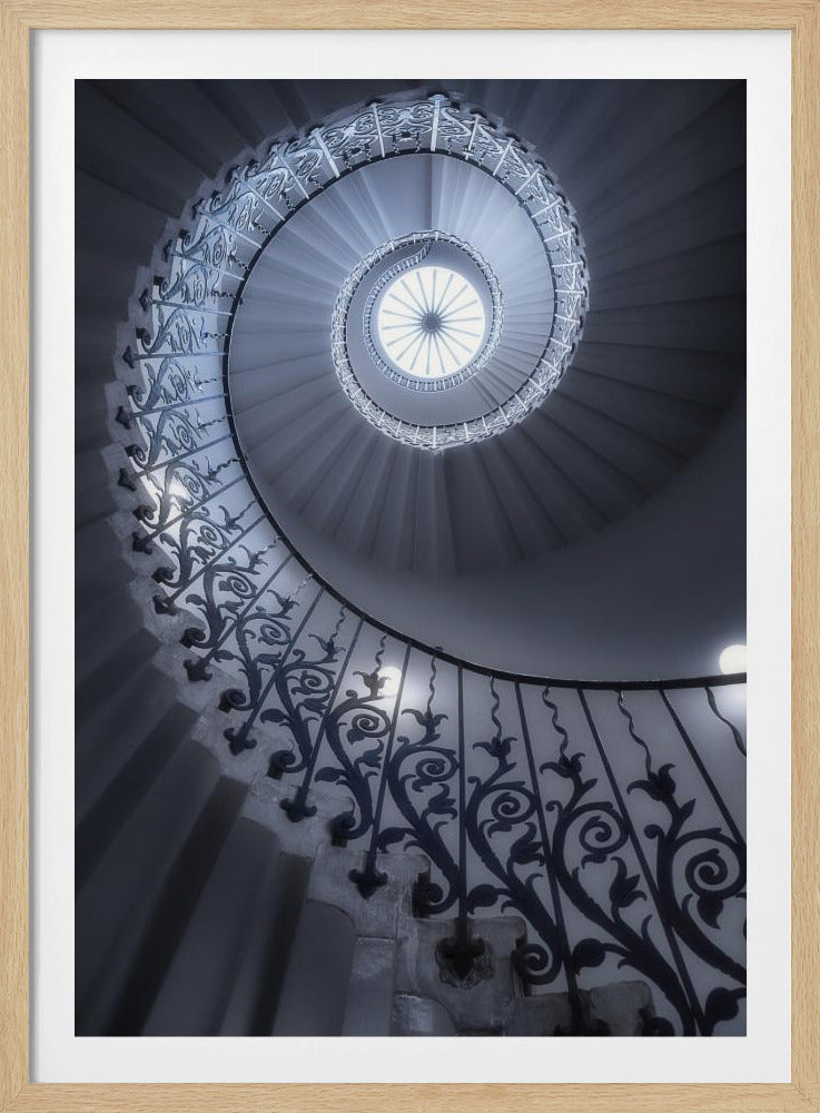 A dramatic low-angle view looking up a majestic spiral staircase, its ornate black wrought iron railings creating a dark, intricate pattern against the cool-toned white steps that wind towards a circular skylight at the apex. Decor