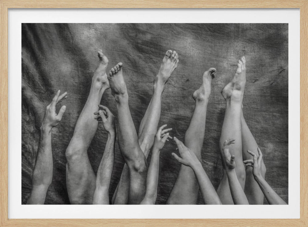 A conceptual black and white photograph in a silver frame, depicting a jumble of multiple human legs, feet, arms, and hands reaching upwards against a dark, textured fabric background. Wall Art