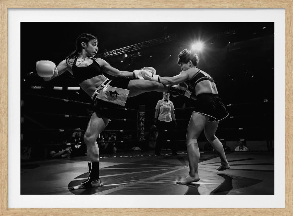 A dramatic black and white action photograph of two female kickboxers in a ring. One fighter, airborne, executes a high kick that connects with the other fighter's gloves, who is bracing for the impact. A referee stands in the background under bright arena lights. Poster