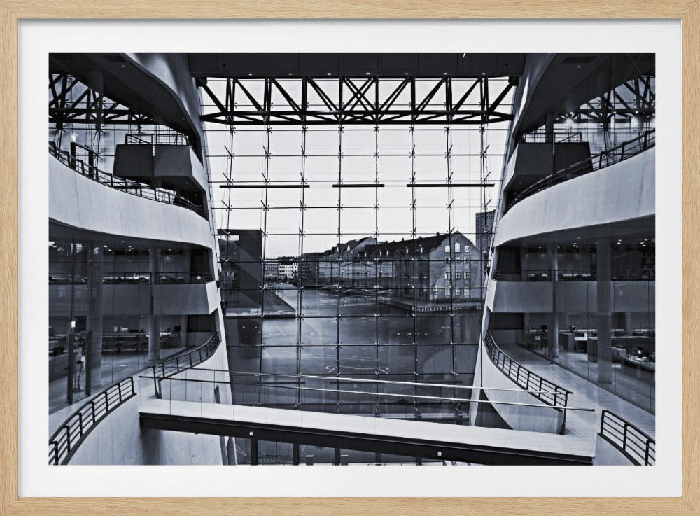 A symmetrical, black and white photograph taken from inside a modern building with curved balconies, looking out through a massive glass wall onto a canal and historic buildings on the opposite bank. A pedestrian bridge crosses the lower part of the frame. Decor
