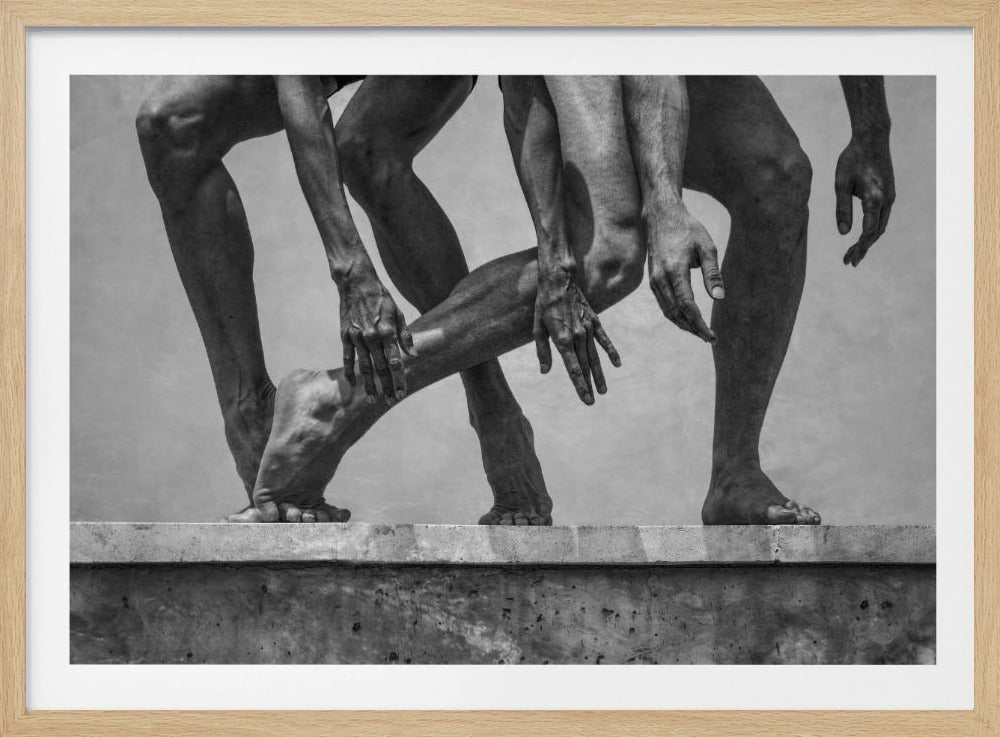 A framed black and white photograph showing a composite image of muscular male legs, arms, and feet in various athletic poses on a concrete ledge. The image focuses on the defined musculature and the dynamic, overlapping arrangement of limbs against a neutral grey background. Print