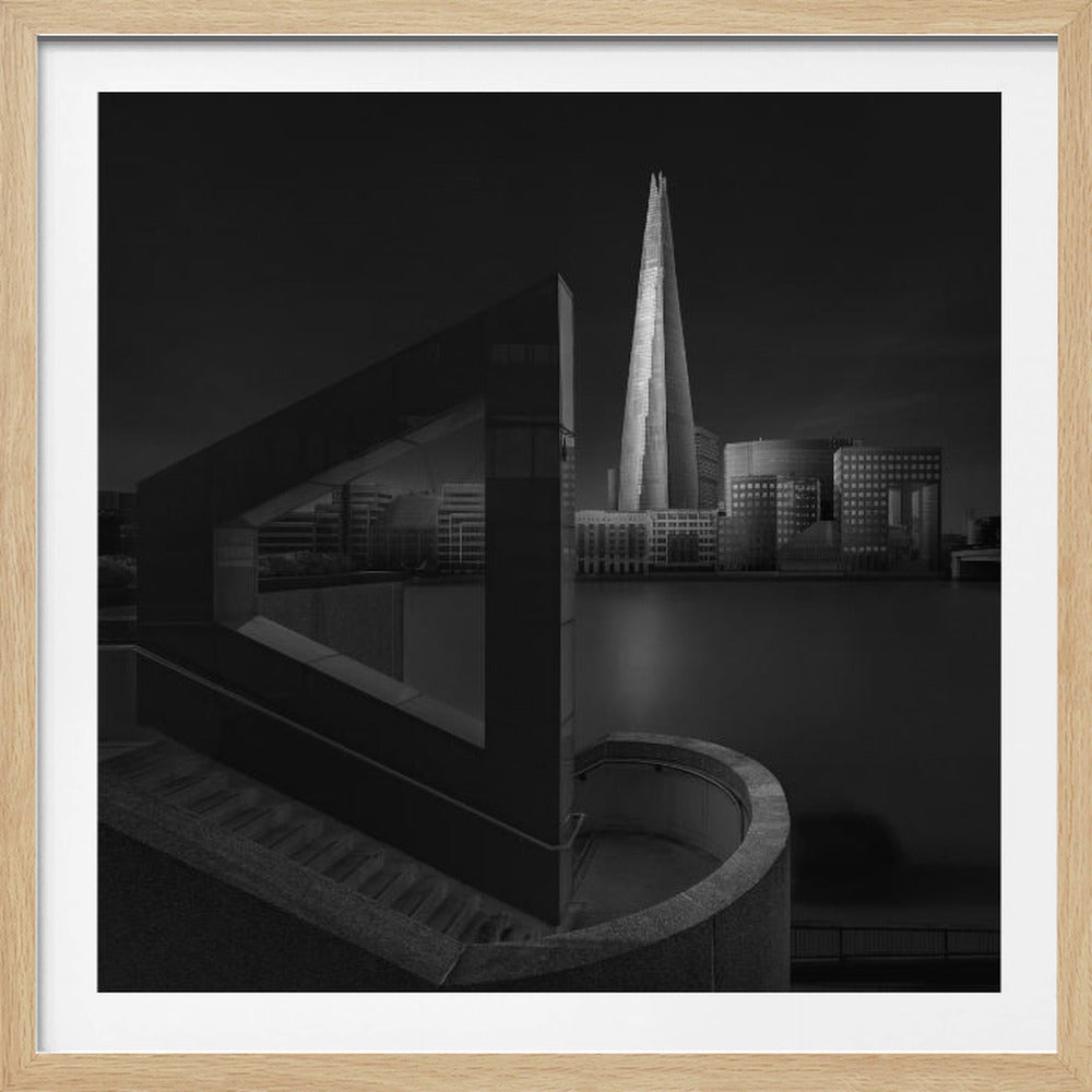 A dramatic black and white architectural photograph of the London skyline at night. The illuminated Shard skyscraper stands tall in the background across a dark river. The foreground features strong geometric shapes, including a large triangular structure and a curved concrete staircase, creating a layered and modern composition. Print