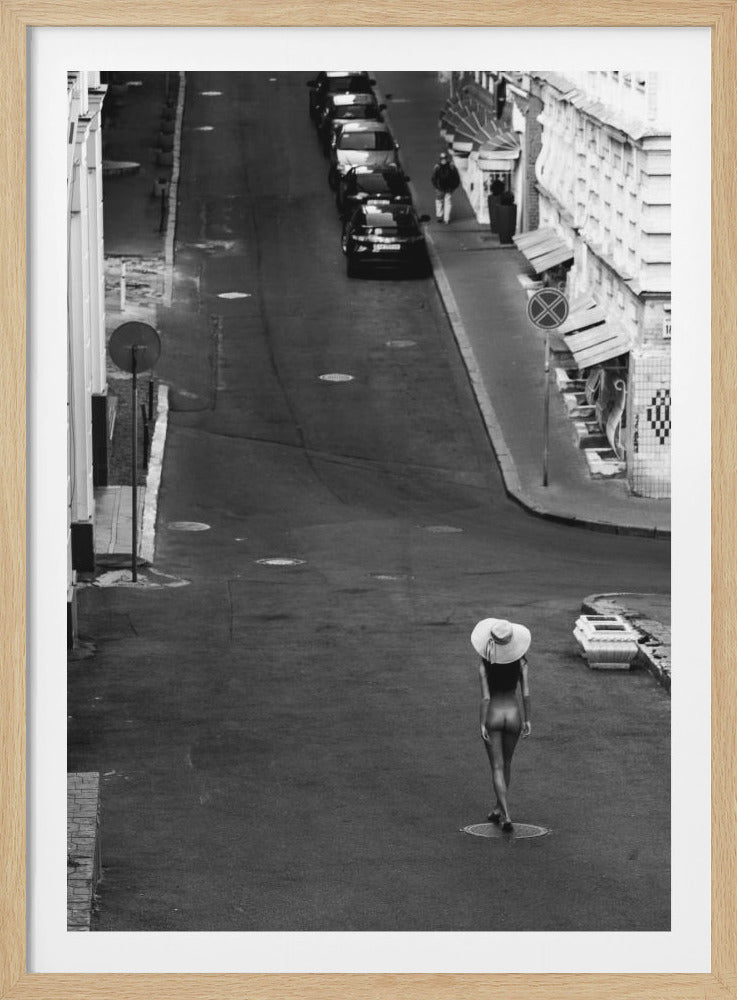 An overhead black and white photograph captures a surreal urban scene. A nude woman, seen from behind and wearing only a large, wide-brimmed hat, walks down the center of a quiet city street lined with parked cars. Print