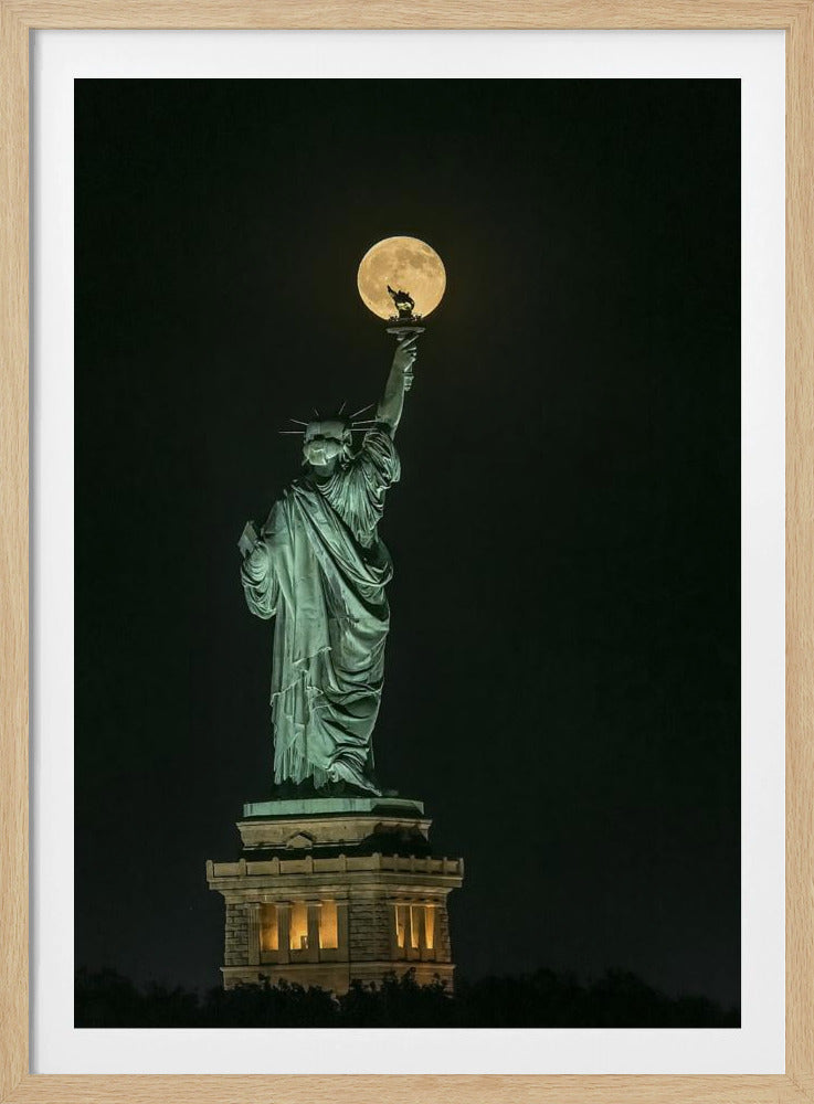A striking night photograph of the Statue of Liberty, where a large, full yellow moon is perfectly aligned behind the torch, creating the illusion that the statue is holding up the moon. Artwork