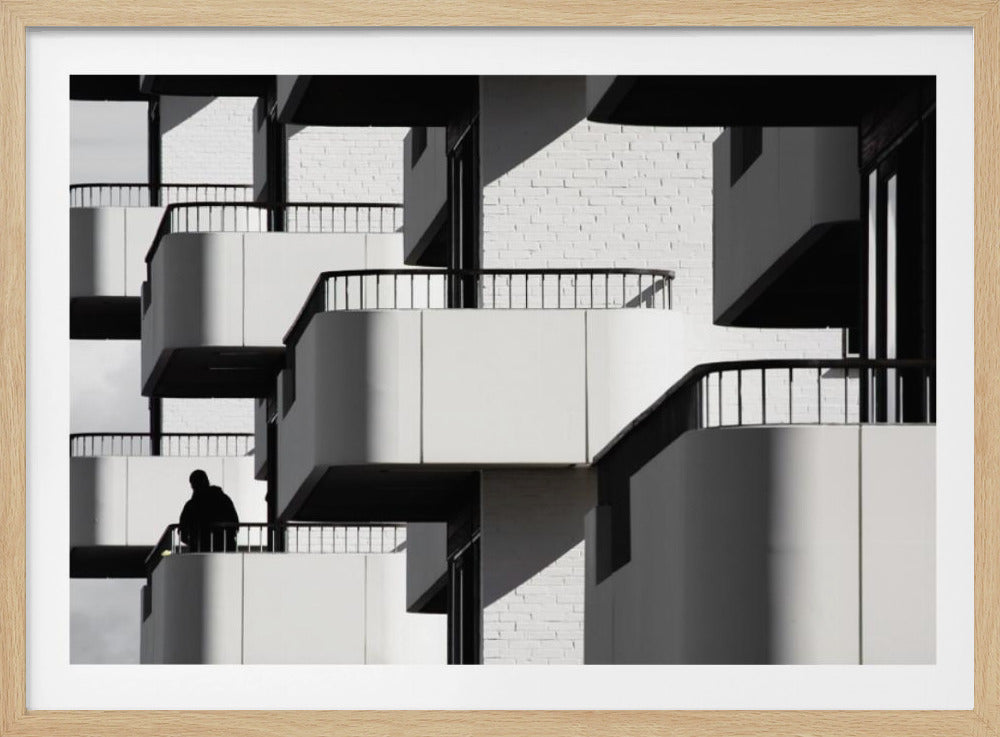 A black and white architectural photograph of a modern building with repeating geometric balconies. Strong sunlight creates deep shadows, emphasizing the lines and curves of the structure. A lone silhouetted figure stands on one of the lower balconies. Decor
