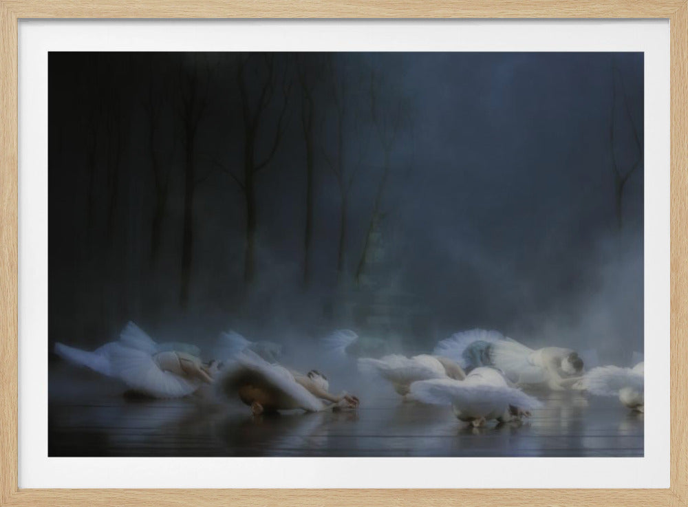 A group of ballerinas in white tutus lie scattered on a reflective stage floor, enveloped in a thick, mysterious fog. In the soft-focused background, the dark silhouettes of bare trees are visible against a deep blue, hazy sky, creating an ethereal and somber atmosphere. Wall Art