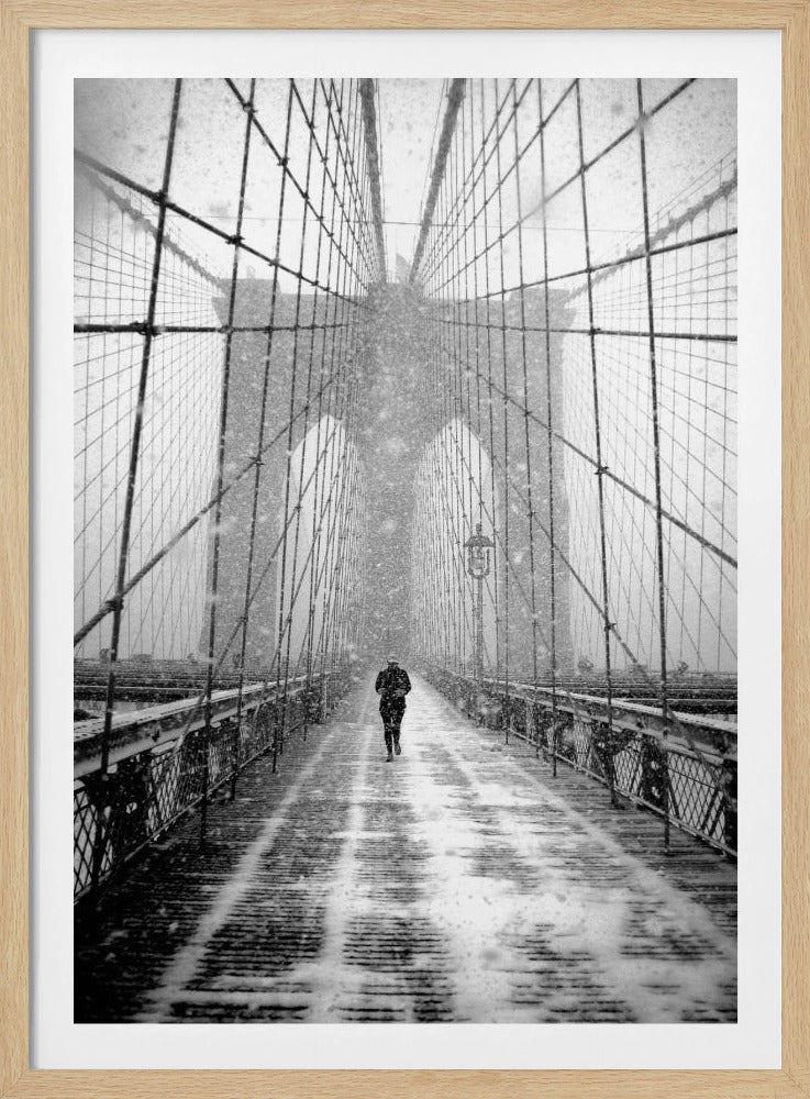 A vertical, black and white photograph of a solitary person walking along the Brooklyn Bridge during a heavy snowstorm. The iconic cables and towers of the bridge create a strong sense of perspective, drawing the eye towards the distant, hazy towers while snow falls all around. Artwork