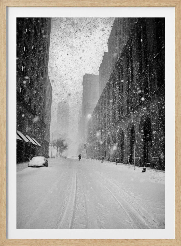 A grainy, black and white photograph captures a deserted city street during a heavy snowstorm. Tall buildings line the street, which is covered in a thick blanket of snow. A single car on the left is almost completely buried, and in the distance, a lone figure walks with an umbrella down the center of the empty road. Poster