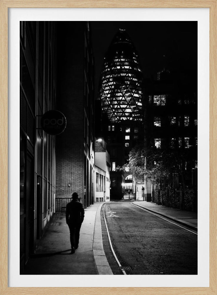 A moody black and white photograph of a person walking away down a narrow, deserted city street at night. In the background, the iconic Gherkin building in London is brightly lit against the dark sky. Wall Art