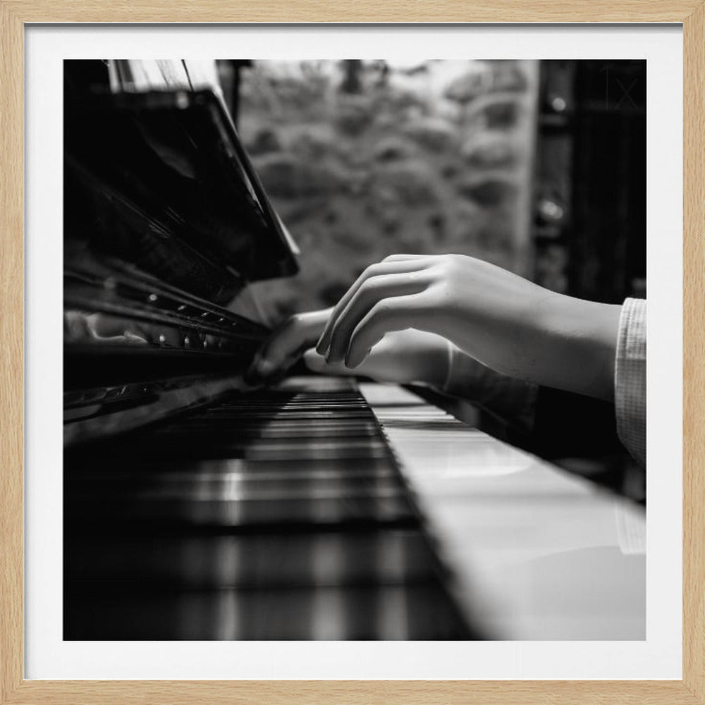 A black and white, low-angle photograph of mannequin hands playing a piano. The focus is on the hands and the keys, with a shallow depth of field blurring the background. The entire image is presented within a light wood frame. Print