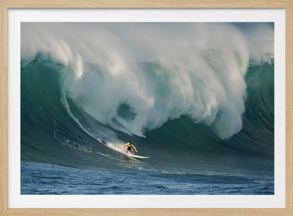 A lone surfer in a yellow shirt rides down the face of an enormous, powerful ocean wave as it crests into white foam, viewed within a silver picture frame. Wall Art