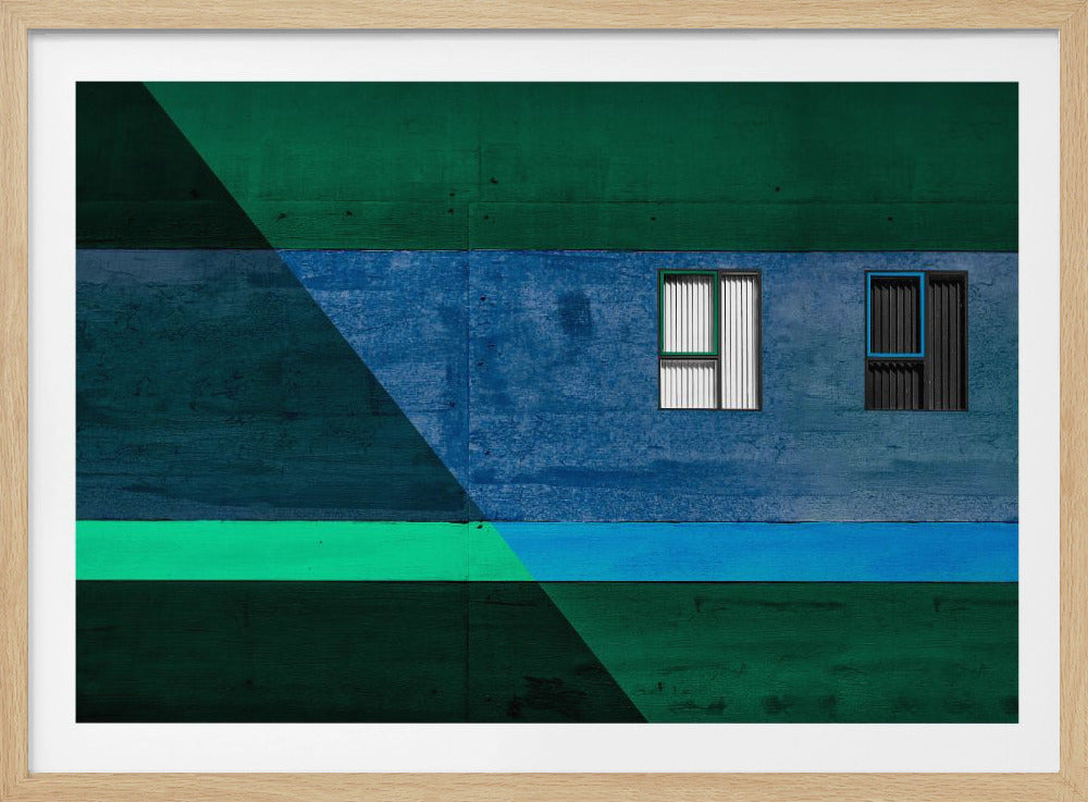 A framed abstract architectural photograph featuring a color-blocked facade. A central horizontal band of textured blue wall contains two small, distinct windows. This is flanked by upper and lower sections of dark green. A large, dark diagonal shape overlays the left side of the composition, creating sharp geometric lines. Decor