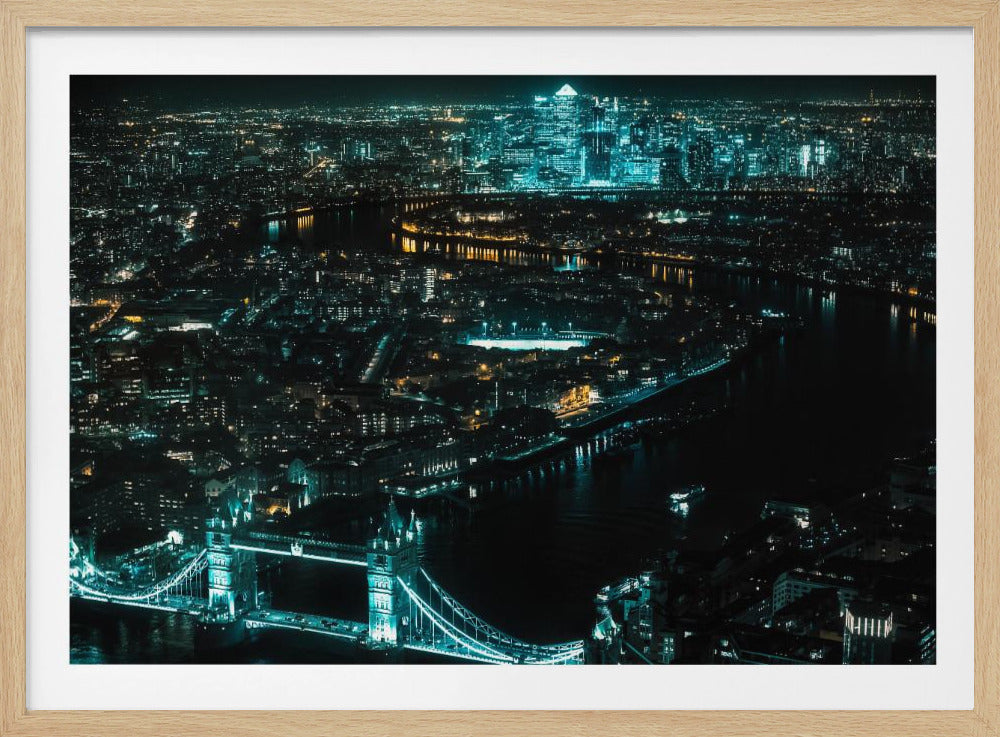 A framed aerial photograph of London at night, featuring the iconic Tower Bridge illuminated in bright teal in the foreground and the glowing skyscrapers of Canary Wharf across the River Thames in the background. Artwork
