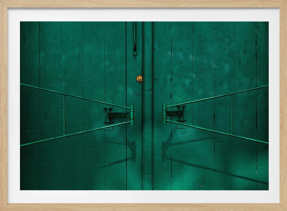 A symmetrical close-up shot of a weathered dark green double door with prominent matching green metal handles and a small brass lock in the center, enclosed in a silver frame. Print